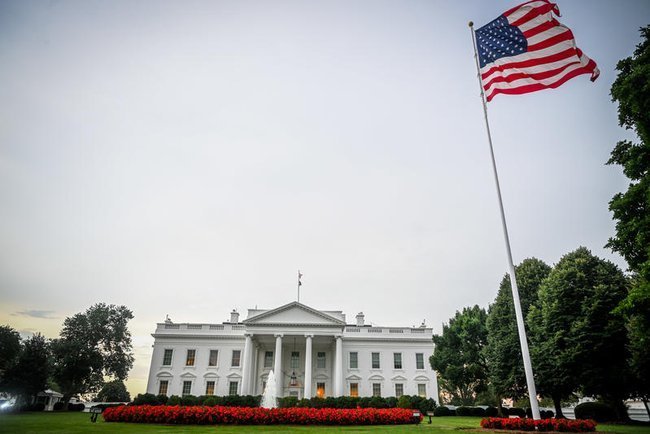 На первом плане американский флаг на флагштоке, за ним Белый дом