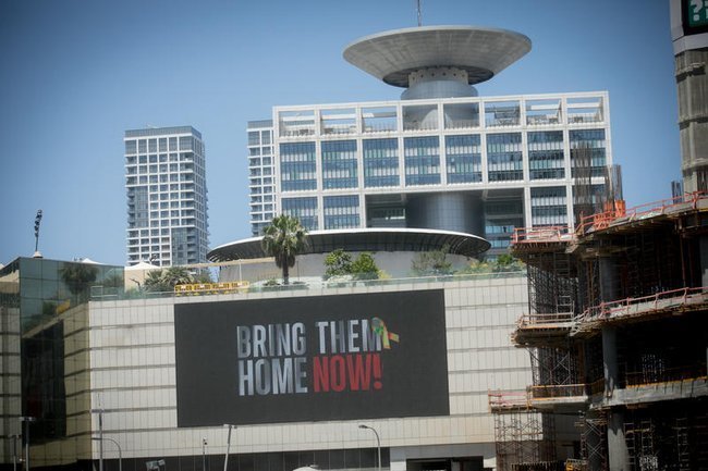 Плакат Bring Them Home Now на фоне здания Кирии в Тель-Авиве