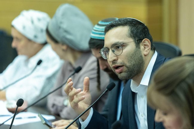 Ицхак Вассерлауф за столом среди людей в кипах говорит в микрофон