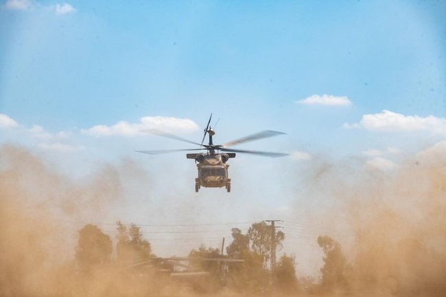 Военный вертолет низко над землей, дорожная пыль