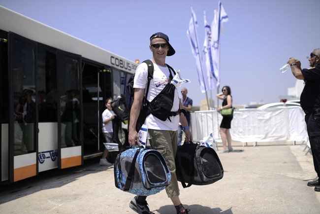 Молодой мужчина-репатриант с сумками на фоне израильского флага