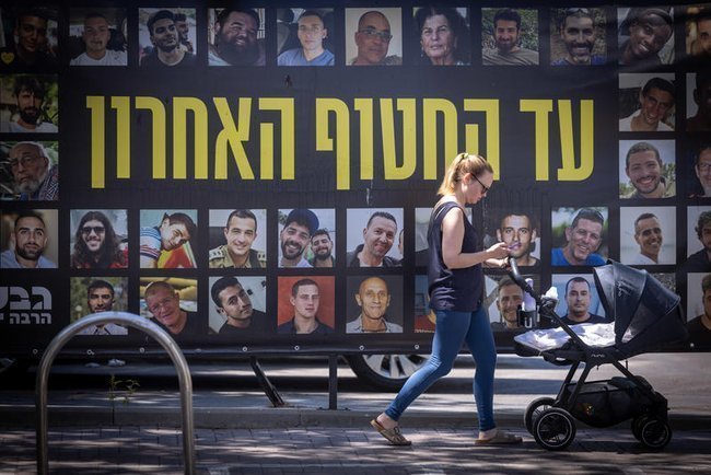 Женщина с коляской на фоне плаката с портретами израильских заложников