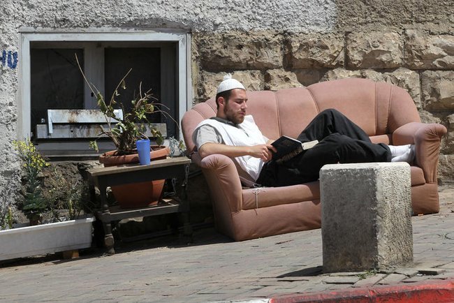 Житель Иерусалима читает книгу, сидя на диване посреди улицы