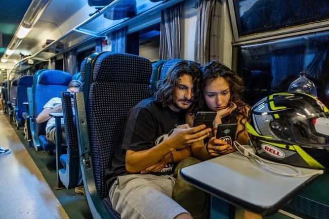 Молодая пара в поезде смотрит в телефоны