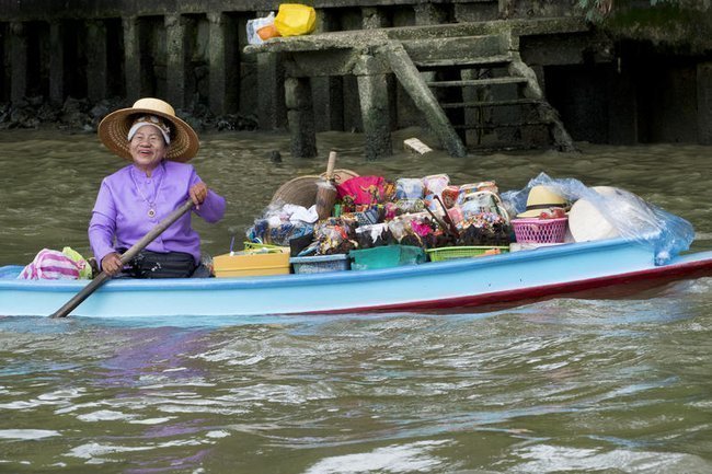 Женщина на лодке, полной фруктов и сувениров, плывет по реке в Бангкоке, Таиланд