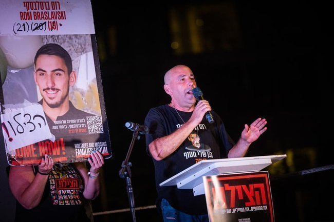 Отец Рома Браславски выступает на площади заложников в Тель-Авиве под портретом сына.