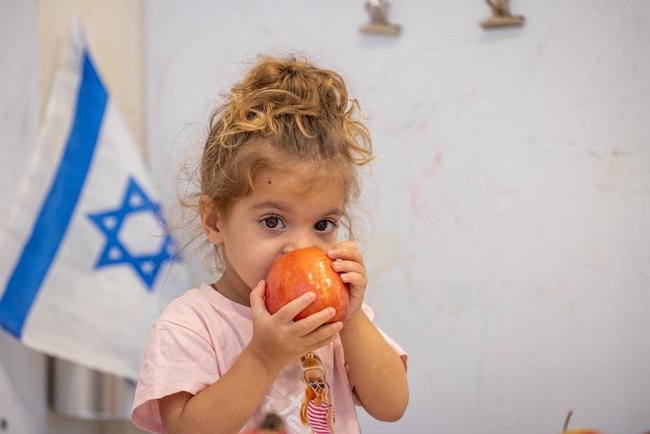 Маленькая девочка ест яблоко в детском саду