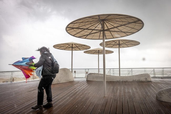 Женщина с зонтом на побережье Тель-Авива во время дождя