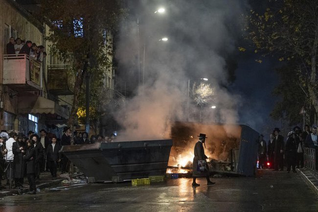 Ультраортодоксальный мужчина идет на фоне пожара во время демонстрации в Иерусалиме