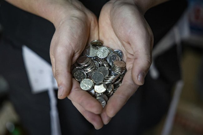 Человек держит в руках монетки в один шекель.