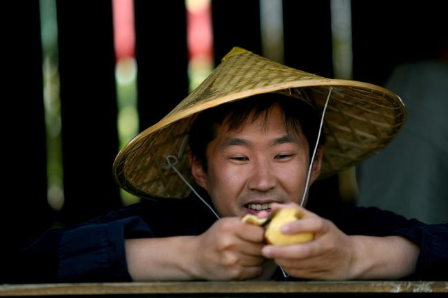 Мужчина в традиционной соломенной шляпе в Китае чистит фрукт