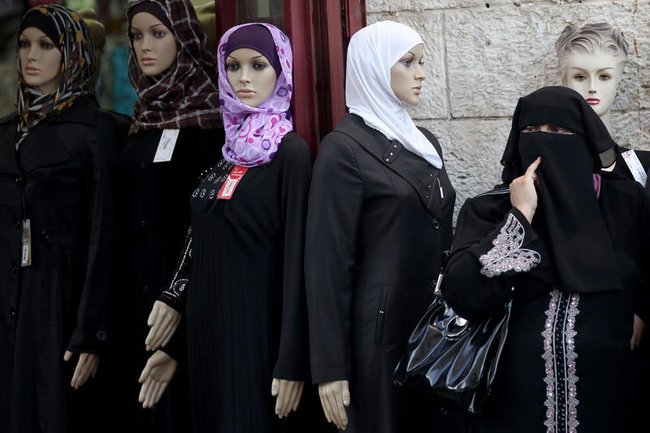 Палестинка в хиджабе на фоне витрины модного магазина.