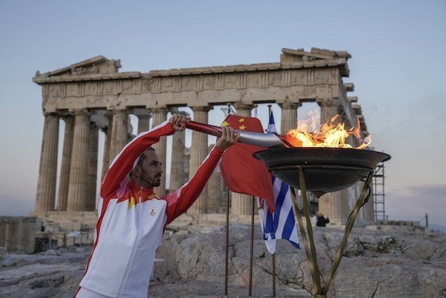Греческий факелоносец, олимпийский чемпион по гимнастике, зажигает олимпийский огонь у Парфенона в Афинах