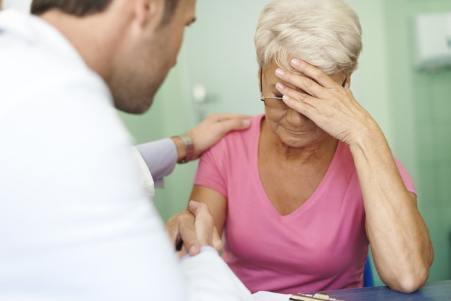 Женщина у которой болит голова обращается за помощью к врачу