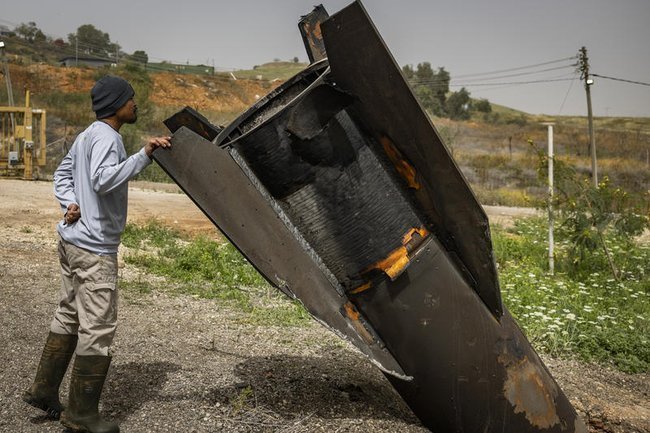 Люди осматривают фрагмент баллистической ракеты, выпущенной из Ирана в сторону Израиля и перехваченной израильскими системами ПВО
