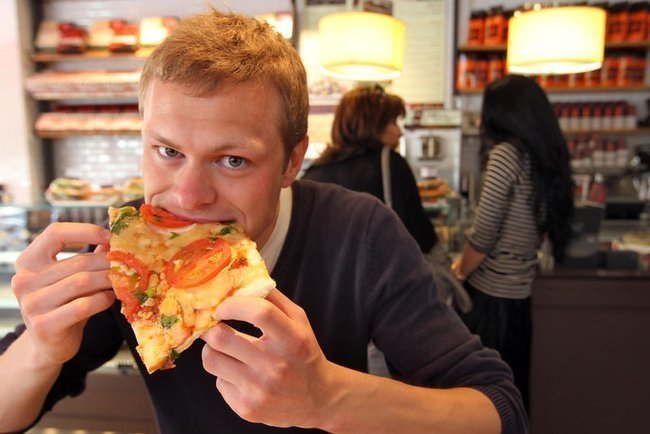 Мужчина ест кусок пиццы в кафе