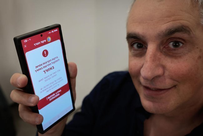 мужчина держит в руках смартфон с оповещением об обстреле